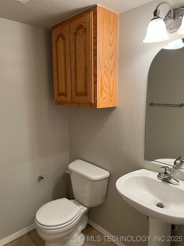 half bathroom with toilet, baseboards, a sink, and a textured ceiling