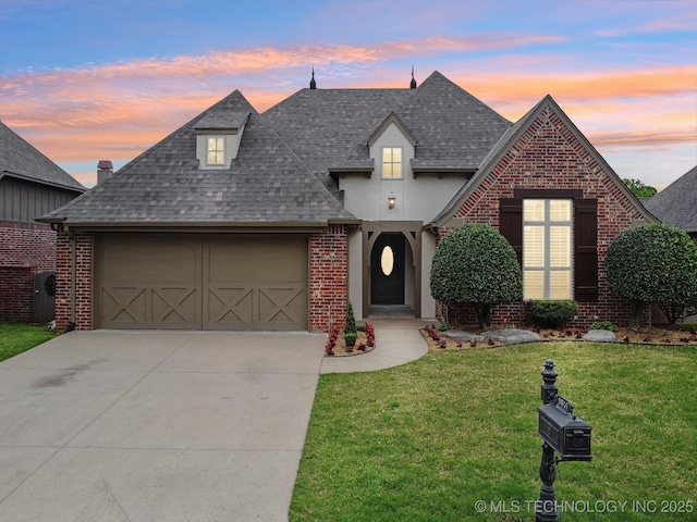 french country style house featuring a shingled roof, a garage, concrete driveway, and a front yard