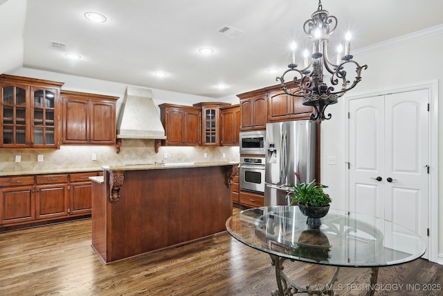 kitchen featuring stainless steel appliances, custom exhaust hood, a chandelier, a kitchen island, and crown molding
