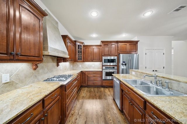 kitchen with stainless steel appliances, a sink, custom range hood, dark wood-style flooring, and glass insert cabinets