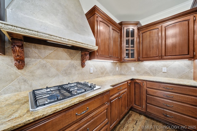 kitchen featuring stainless steel gas cooktop, light stone countertops, glass insert cabinets, and crown molding