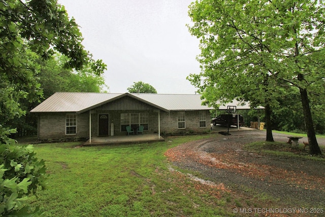 rear view of house with a lawn, dirt driveway, metal roof, and covered porch