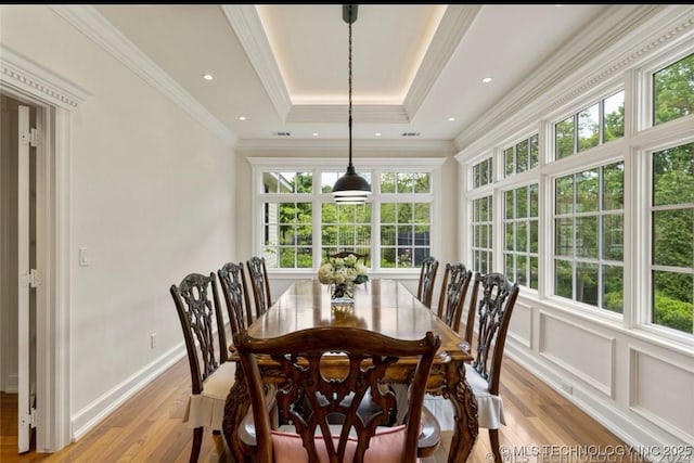 dining area featuring ornamental molding, light wood finished floors, and a tray ceiling