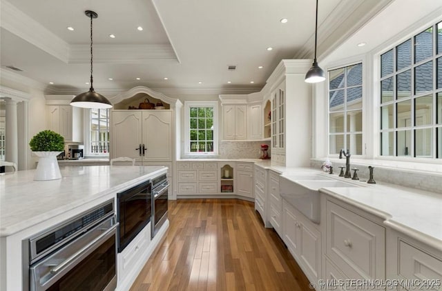 kitchen featuring a tray ceiling, backsplash, a sink, light wood finished floors, and stainless steel oven