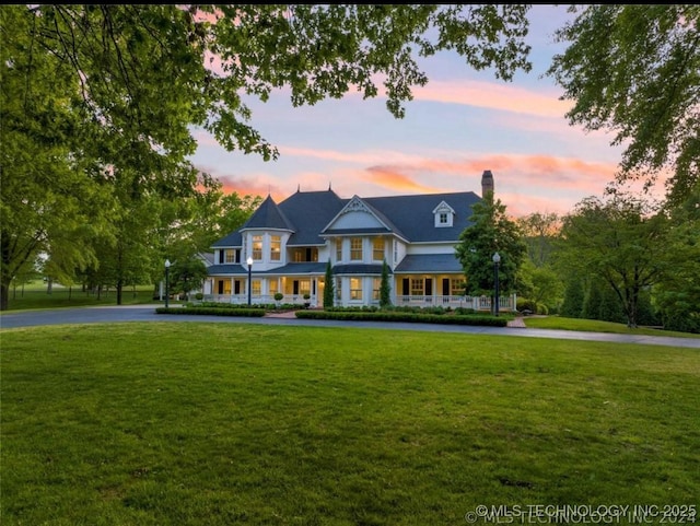 victorian home with curved driveway, a front yard, a chimney, and a porch