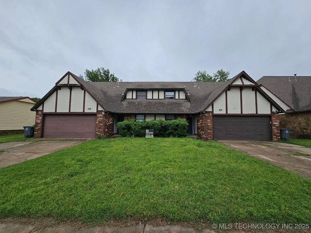tudor home featuring an attached garage, driveway, brick siding, and a front yard