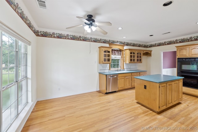 kitchen with a sink, light wood finished floors, dobule oven black, stainless steel dishwasher, and glass insert cabinets