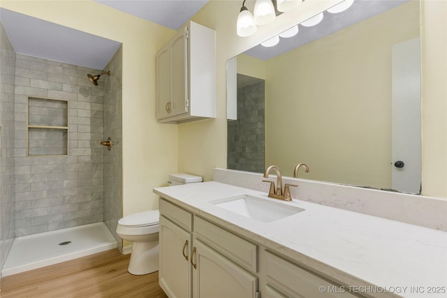 full bath featuring vanity, wood finished floors, a tile shower, and toilet
