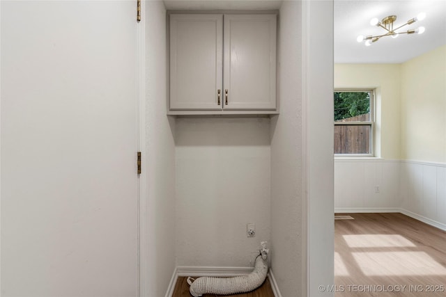 laundry area with hookup for an electric dryer, an inviting chandelier, cabinet space, a wainscoted wall, and light wood-style floors