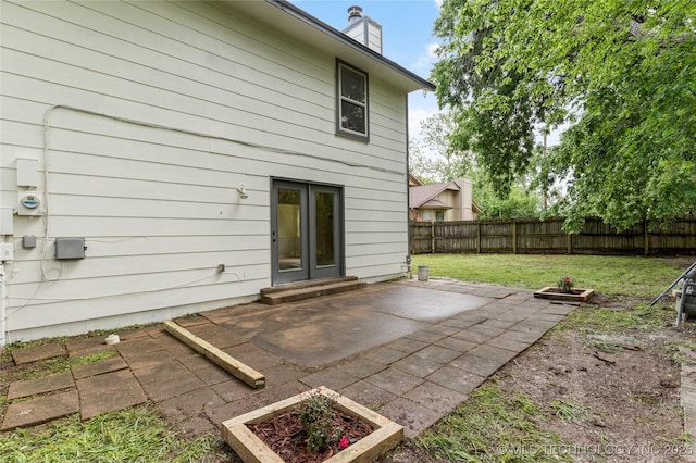 back of house with french doors, a fenced backyard, a chimney, a patio area, and a lawn