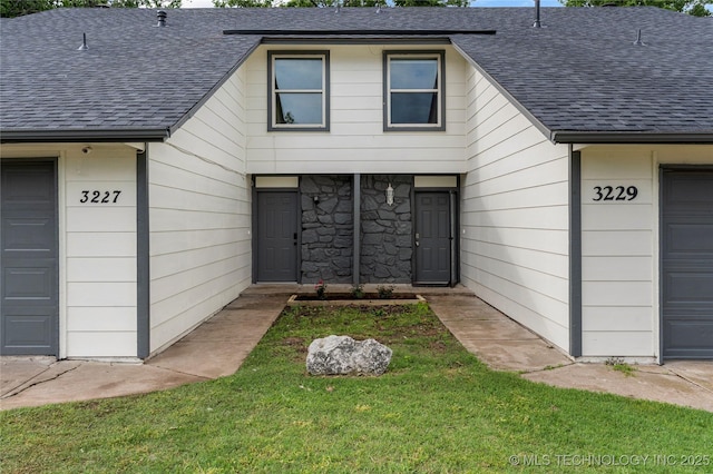 property entrance featuring a lawn, a shingled roof, and stone siding