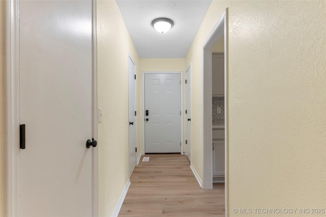 hall featuring baseboards, a textured wall, and light wood-type flooring