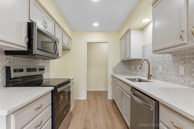 kitchen featuring appliances with stainless steel finishes, tasteful backsplash, a sink, light stone counters, and light wood-style flooring