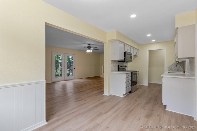kitchen with appliances with stainless steel finishes, a sink, light countertops, a ceiling fan, and light wood-type flooring