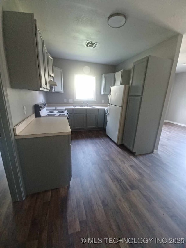 kitchen featuring dark wood-style flooring, visible vents, electric range oven, light countertops, and freestanding refrigerator