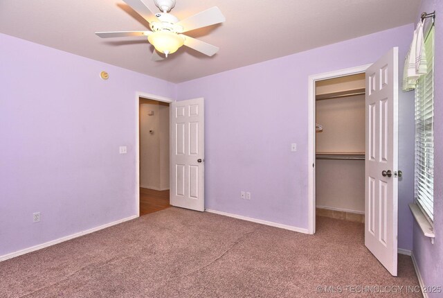 unfurnished bedroom with a closet, baseboards, a walk in closet, ceiling fan, and carpet