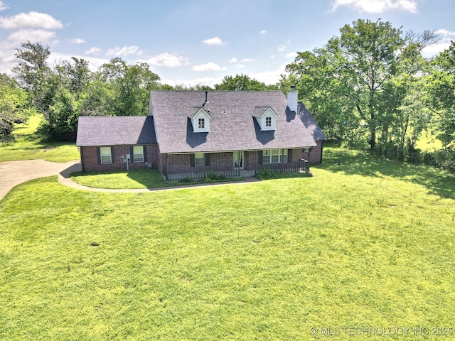cape cod house featuring a front lawn, roof with shingles, a chimney, brick siding, and a porch
