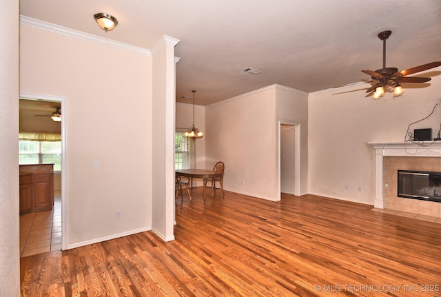 unfurnished living room featuring ornamental molding, ceiling fan with notable chandelier, wood finished floors, and a fireplace