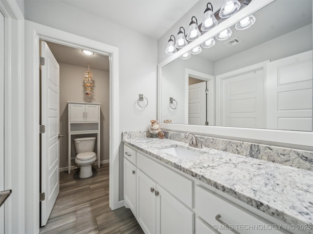 bathroom with vanity, toilet, baseboards, wood finished floors, and visible vents