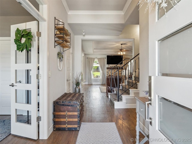 entrance foyer with a ceiling fan, crown molding, baseboards, dark wood-style floors, and stairs