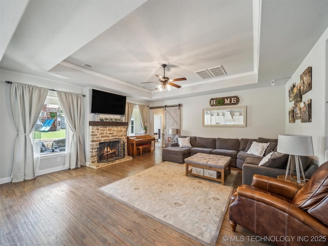 living area featuring visible vents, a barn door, a ceiling fan, and a tray ceiling