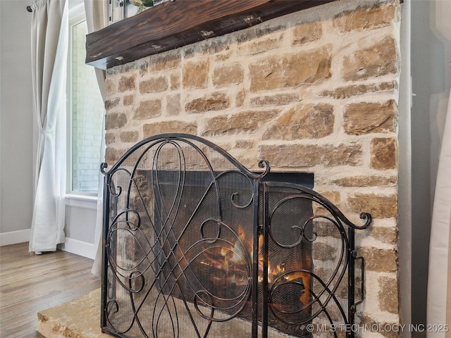 interior details with a stone fireplace, baseboards, and wood finished floors