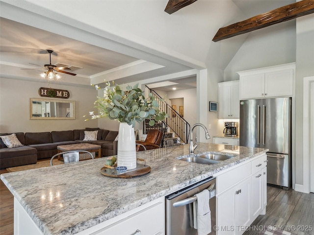 kitchen featuring open floor plan, light stone counters, a sink, dark wood finished floors, and stainless steel appliances