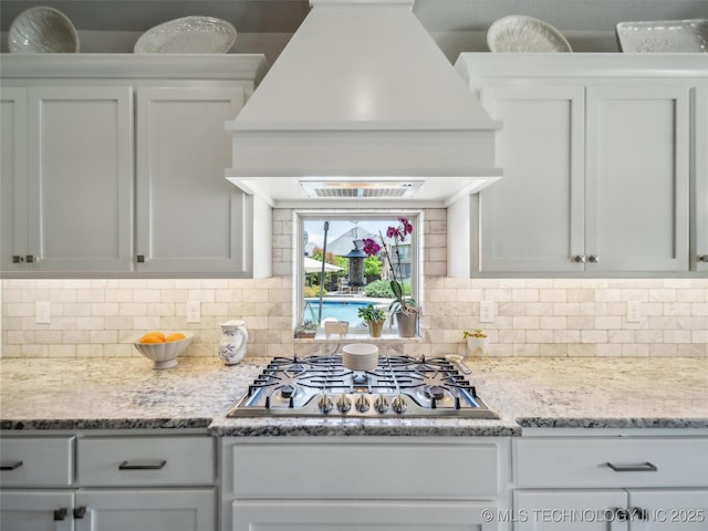 kitchen with decorative backsplash, white cabinets, stainless steel gas cooktop, and premium range hood