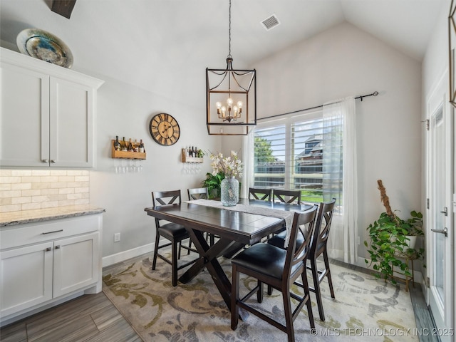 dining area featuring light wood finished floors, a chandelier, baseboards, lofted ceiling, and visible vents
