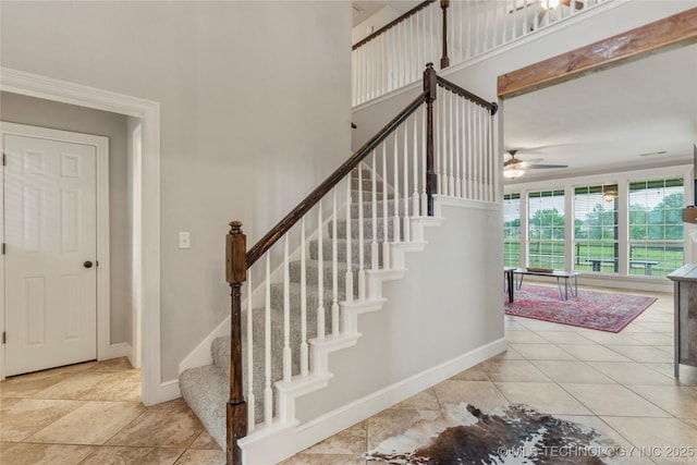 stairs with a ceiling fan, baseboards, and a towering ceiling