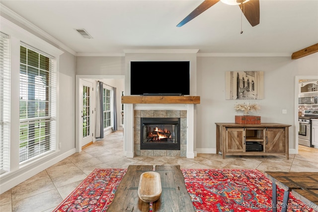 living room featuring baseboards, ceiling fan, ornamental molding, and a tiled fireplace