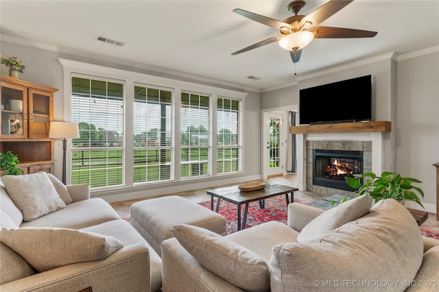 living area with a ceiling fan, visible vents, crown molding, a tile fireplace, and baseboards