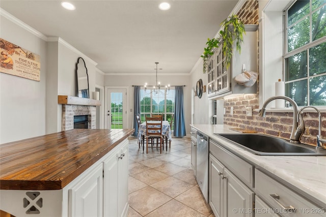 kitchen featuring stainless steel dishwasher, a fireplace, a sink, wood counters, and backsplash