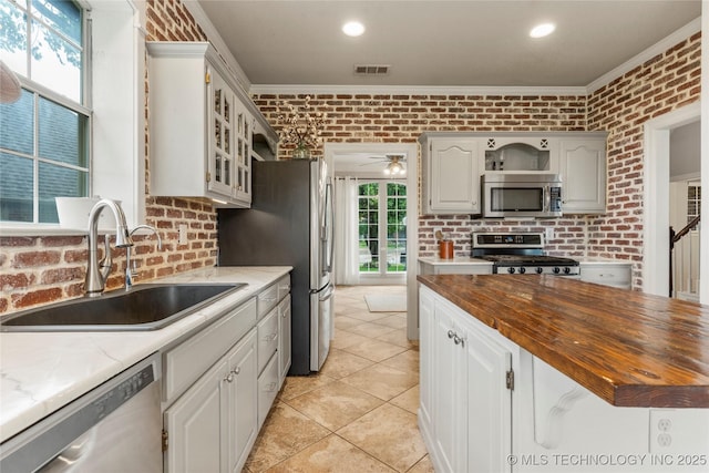 kitchen with visible vents, butcher block counters, brick wall, a sink, and stainless steel appliances