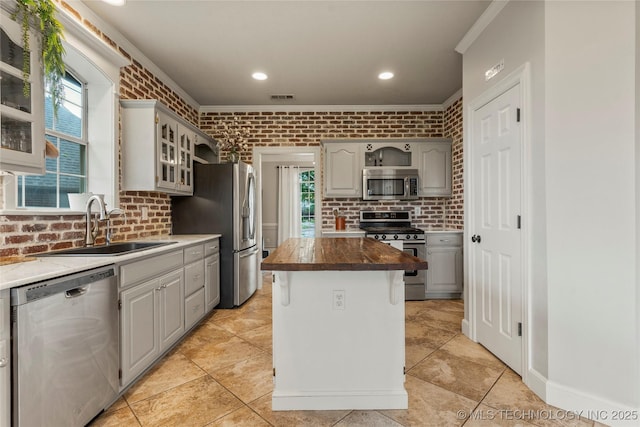 kitchen with crown molding, brick wall, glass insert cabinets, a sink, and stainless steel appliances