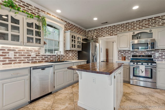 kitchen featuring brick wall, crown molding, appliances with stainless steel finishes, a sink, and glass insert cabinets