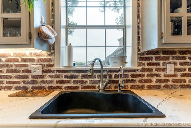 room details featuring a sink, glass insert cabinets, and light stone countertops
