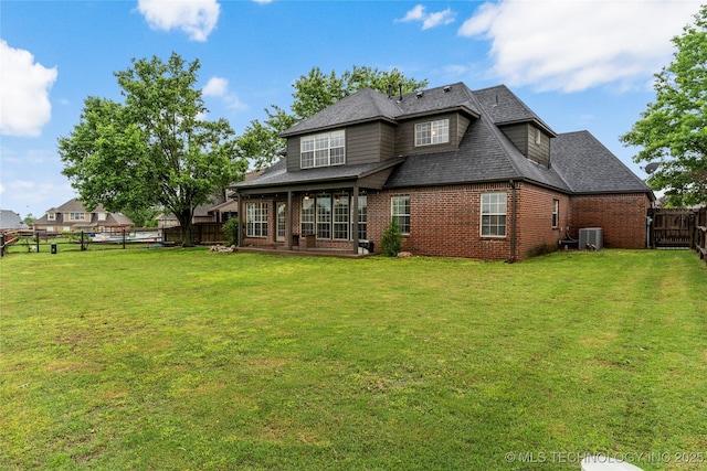 rear view of house with a shingled roof, brick siding, a fenced backyard, central air condition unit, and a yard