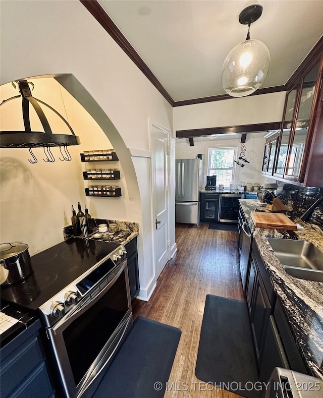 kitchen featuring crown molding, appliances with stainless steel finishes, wood finished floors, a sink, and glass insert cabinets