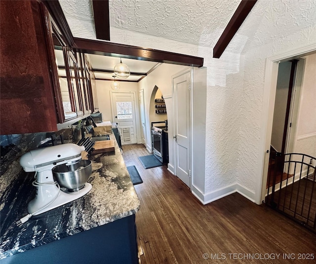 kitchen with arched walkways, baseboards, dark wood-style floors, stainless steel electric stove, and a textured wall