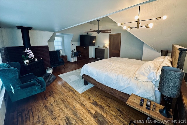 bedroom with a notable chandelier, vaulted ceiling, wood finished floors, and a wood stove
