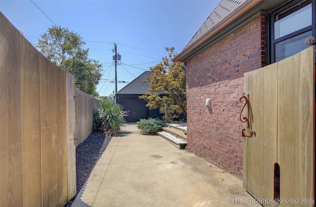 view of side of property with a garage, fence, brick siding, a patio area, and an outbuilding