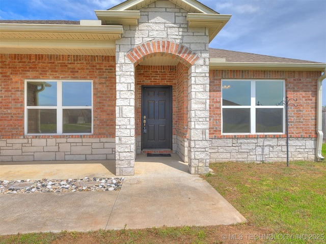 view of exterior entry featuring stone siding, brick siding, and roof with shingles