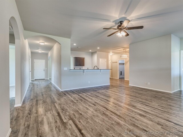 unfurnished living room with a ceiling fan, baseboards, and wood finished floors