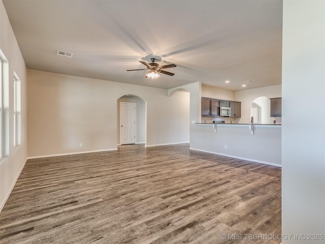 unfurnished living room with arched walkways, dark wood finished floors, visible vents, and a ceiling fan