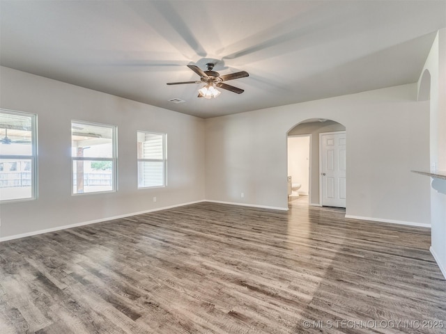 unfurnished living room featuring wood finished floors, visible vents, ceiling fan, arched walkways, and baseboards