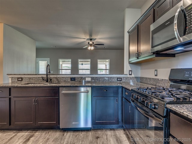 kitchen featuring light wood finished floors, ceiling fan, a sink, dark stone counters, and appliances with stainless steel finishes