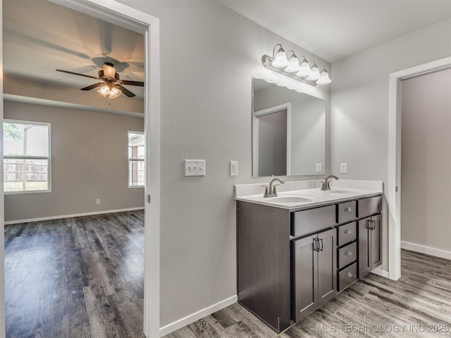 bathroom featuring a ceiling fan, double vanity, a sink, and wood finished floors