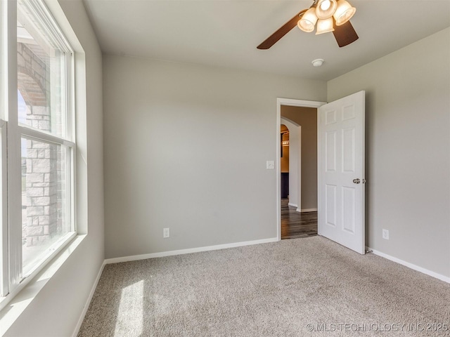 carpeted spare room featuring arched walkways, a ceiling fan, and baseboards