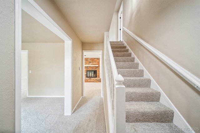 staircase featuring baseboards, a fireplace, and carpet flooring